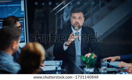 Corporate Meeting Room: Sitting at the Conference Table Charismatic Director Talks Enthusiastically and Gesticulates Energetically proving His point to Investors, Lawyers, Executives Royalty-Free Stock Photo #1731140848