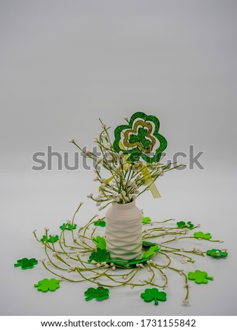 A picture of clover-shaped pop with decorative plants in a white vase    surrounded by green ornamental shamrocks against a grey background
