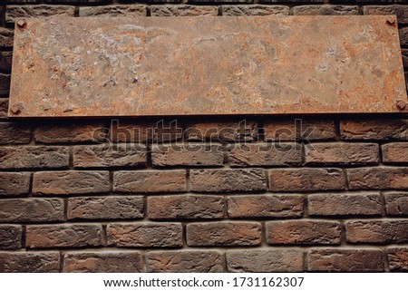 Pattern of an old empty metal sign on a brown brick wall. The sign looks expensive.