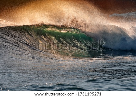 Green blue ocean splashing wave in front of orange sunset sky background. Perfect wave for surfing