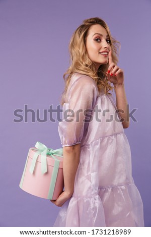 Image of happy caucasian woman with gift box making silence gesture isolated over purple background
