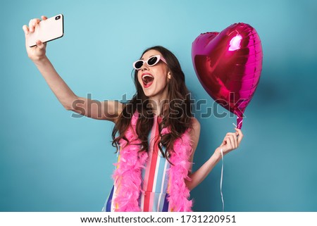 Image of joyful brunette woman taking selfie on cellphone and holding balloon isolated over blue background