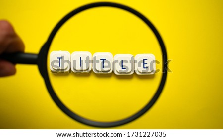 A magnifying glass looking to the word "title" made with letter game blocks on a bright yellow background. Conceptual image of the importance of the title in the searching engines Royalty-Free Stock Photo #1731227035