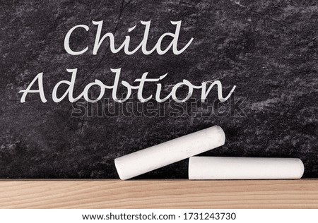 Pieces of white chalk and phrase CHILD ADOPTION on blackboard, top view