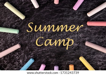 Text Summer camp written with chalk on chalkboard, and some chalk sticks of different colors