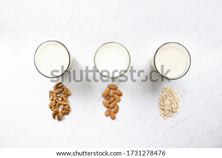 Almond, walnut, oat milk on marble background top view. Nut milk vegan lactose-free, dairy free milk drink. Health diet and nutrition. Stock photo.