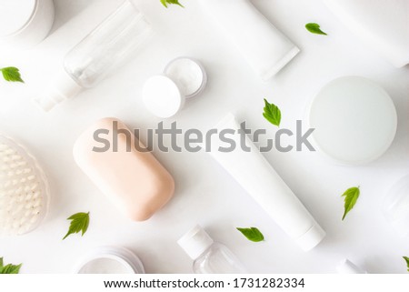 White squeeze tube, bottle of cream, shampoo, soap, cleanser, body brush, empty container flat lay with green leaves on white background top view. Beauty skincare, natural cosmetic. Stock photo