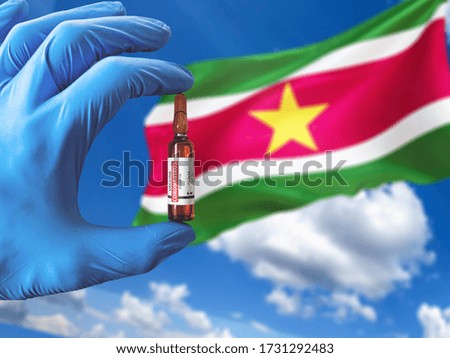 Suriname  flag with Coronavirus Covid-19 concept. Doctor with blue protection medical gloves holding a vaccine bottle. Epidemic Virus, Cov-19, Corona virus outbreaking.3D illustration.