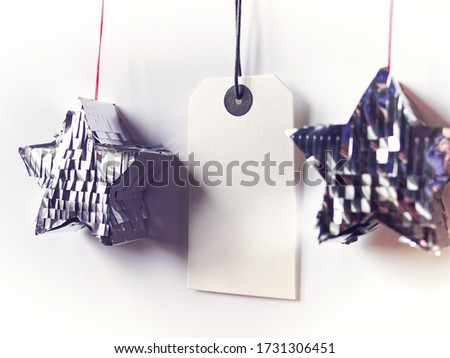 An empty paper price tag hangs on a rope along with decorative stars. Sales season. Copy space. White bakround.