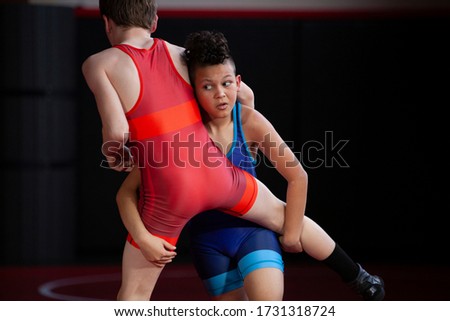 Youth wrestlers drilling takedowns wearing blue and red singlets