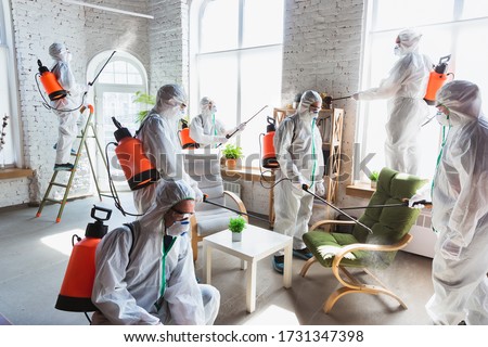 Coronavirus Pandemic. A disinfectors in a protective suit and mask sprays disinfectants in house or office. Protection against COVID-19 disease. Prevention of spreding pneumonia virus with surfaces. Royalty-Free Stock Photo #1731347398