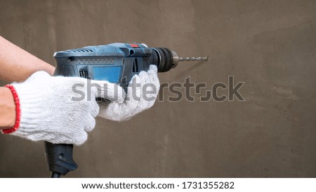 Picture of the hand of a technician who is using a drill to drill the cement wall.