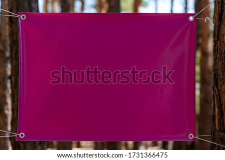 Blank red canvas with copy space for your text message or content for advertising, stretched between two trees/Empty vinyl canvas on the blurred background outdoor