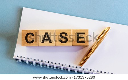 word CASE written in letters on wooden cube blockson a white notebook with golden pen on a blue table