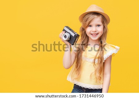 Portrait of a happy child a little blonde girl with long hair on a Colored yellow background with a retro camera in her hands. The concept of rest, travel. 