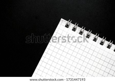 Fragment of a checkered notebook on a black background close-up. Top view. Office concept