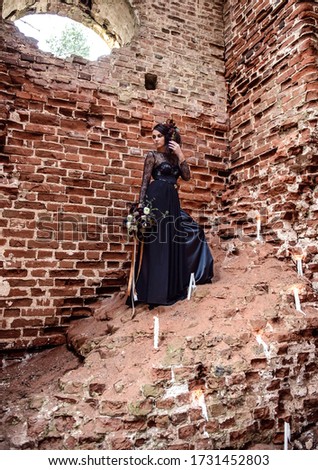 A woman in a black dress on the background of old red brick ruins
