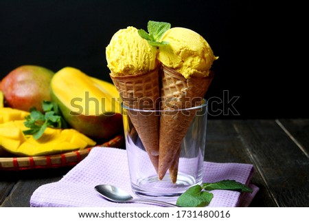 Mango Ice Cream In Waffle Cones In Glass On Napkin And Fresh Mango Fruit Sliced On Plate On Dark Background. Side View.