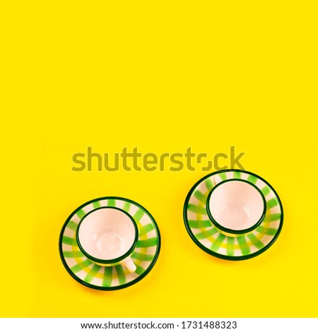 Beautiful little green striped two tea coffee cups and saucers on a yellow background. The concept of home tea drinking, comfort. Square.