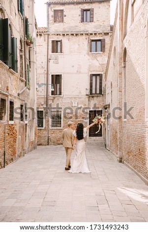 Italy wedding in Venice. The bride and groom walk along the deserted streets of the city. Newlyweds are walking in a dead end alley on the background of brick buildings.
