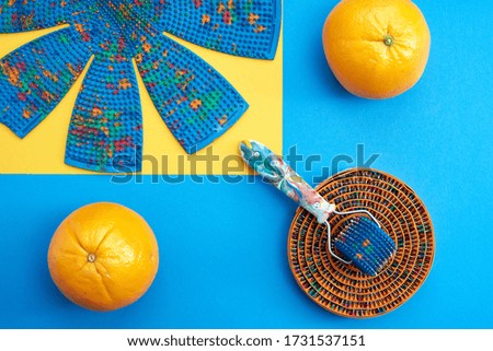 Massager in the form of chamomile, with roller, and ribbon type, with metal needles of different types lie on the blue surface near oranges. top view. Subject and promotional photography. For