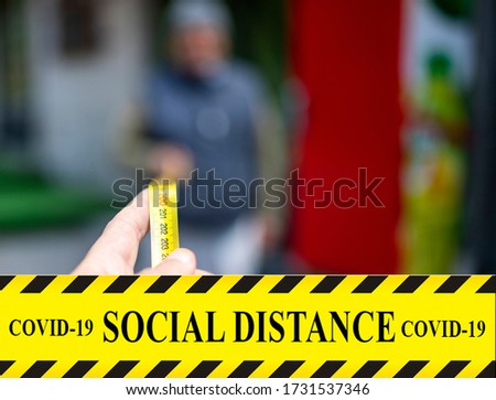 Hand holding a meter. Yellow ribbon with text "social distance covid-19".