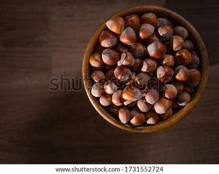 Picture of a bowl full of hazelnuts on the brown wooden table.