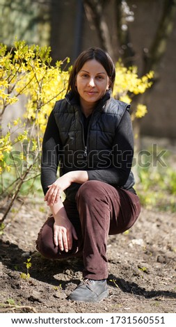 Beautiful woman in black jacket and brown pants in a park in spring. Woman squatting