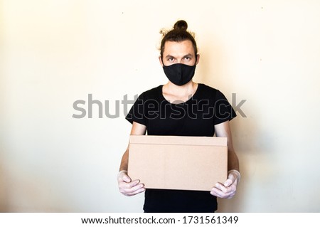 A man wear protective face mask and gloves holding cardboard box. Delivery service and volunteering during pandemic coronavirus concept.