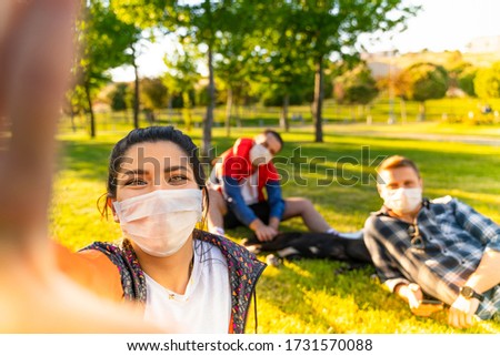 Cheerful university student taking selfie with friends sitting on grass