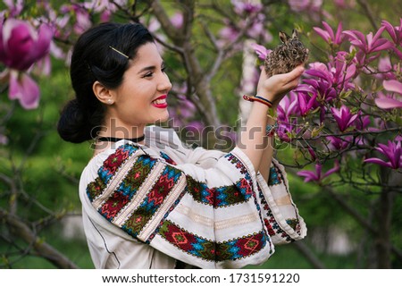 Beautiful young woman posing in romanian traditional costume with a little rabbit in a magnolia orchard