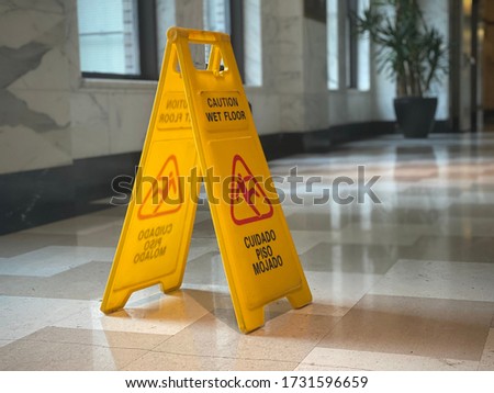 LOS ANGELES, CA, APR 2020: close up on yellow "Caution, Wet Floor" sign in marble-tiled lobby with daylight coming from windows at side.