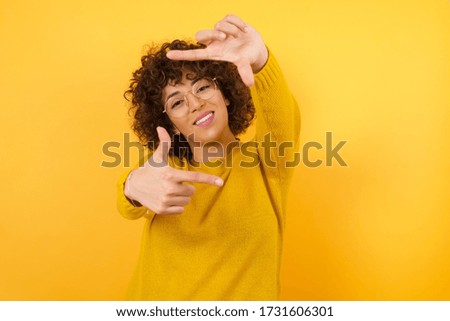 Young beautiful smiling brunette girl wearing casual yellow sweater making finger frame with hands. Creativity and photography concept.