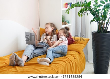 Two sisters lying on a bed together using laptop watching something 