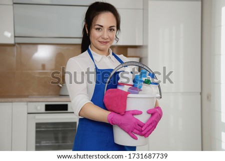Girls with a bucket in their hands. Bucket of detergents. Against the background of a white beautiful modern kitchen.