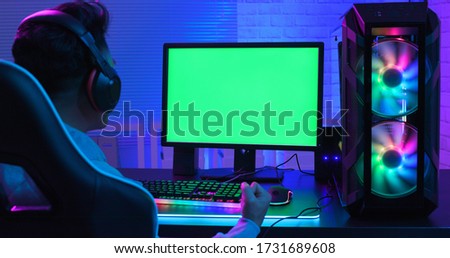 E Cyber sport gamer has fist gesture in front of green screen monitor with powerful personal computer on the table at home