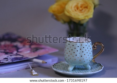 journal, pen beside green porcelain coffee cup and yellow roses in vase.
