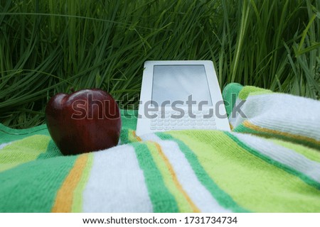An e-reader and an apple in the grass
