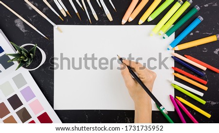 Top view of black desktop with piece of white paper and various colorful drawing tools. Royalty-Free Stock Photo #1731735952
