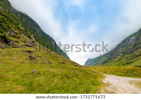 Steep rocky mountains with low green grass, dirt road and wet stones during a cool summer day in the norwegian countyside. Scenic nature view. Travel and tourism photography, outdoor activity.