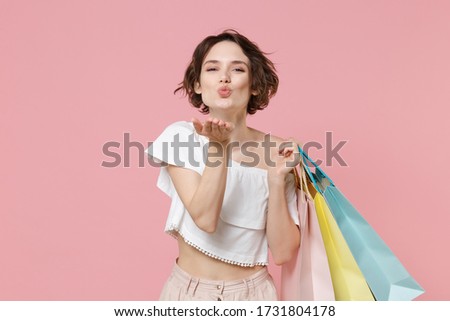 Pretty young woman girl in summer clothes hold package bag with purchases isolated on pink background studio portrait. Shopping discount sale concept. Mock up copy space. Blowing sending air kiss