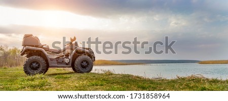 Beautiful nature landscape with unknown ATV awd quadbike motorcycle near lake or river pond coast and cloudscape sky background. Offroad adventure trip . Extreme sport activity panoranic wide view