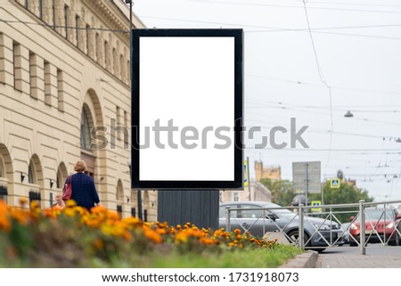 billboard in the city in front of a flower bed in the city with people passing by