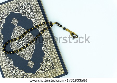 Holy Al Quran with written arabic calligraphy meaning of Al Quran with rosary over white background                 