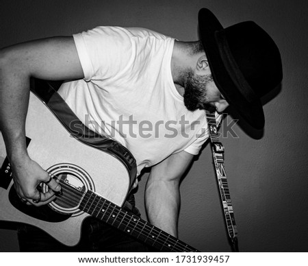 Young man with a white t-shirt, a hat and vintage rings playing an acoustic guitar passionately. Selective focus. Flash. B&W.