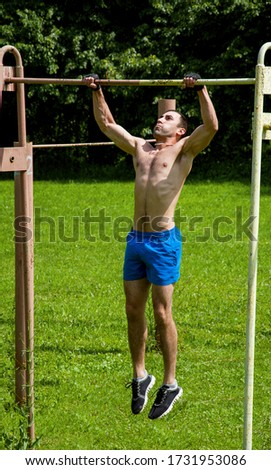 A young man is pulling up on a crossbar, on a street sports field, on a Sunny summer day.