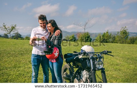 Young couple looking mobile with a motorcycle outdoors