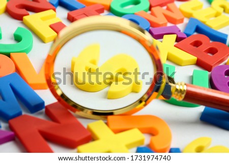 Magnifying glass over dollar sign surrounded by magnet letters on white background, closeup. Search concept