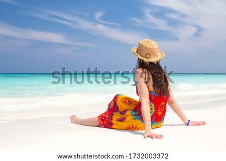 Beautiful women wear brightly colored dresses, and wear weave wooden hats sitting on the white sandy beach, the sea overlooking blue horizon and clear sky at tropical Island in Thailand