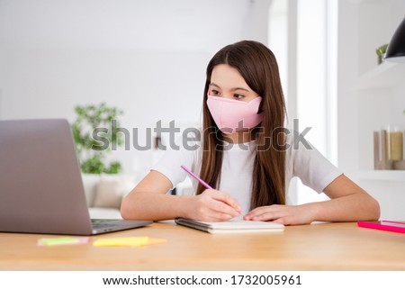Photo of little pretty pupil small school lady laptop notebook table online lesson sit desk use safety facial mask write teacher notes distance quarantine study comfort living room indoors